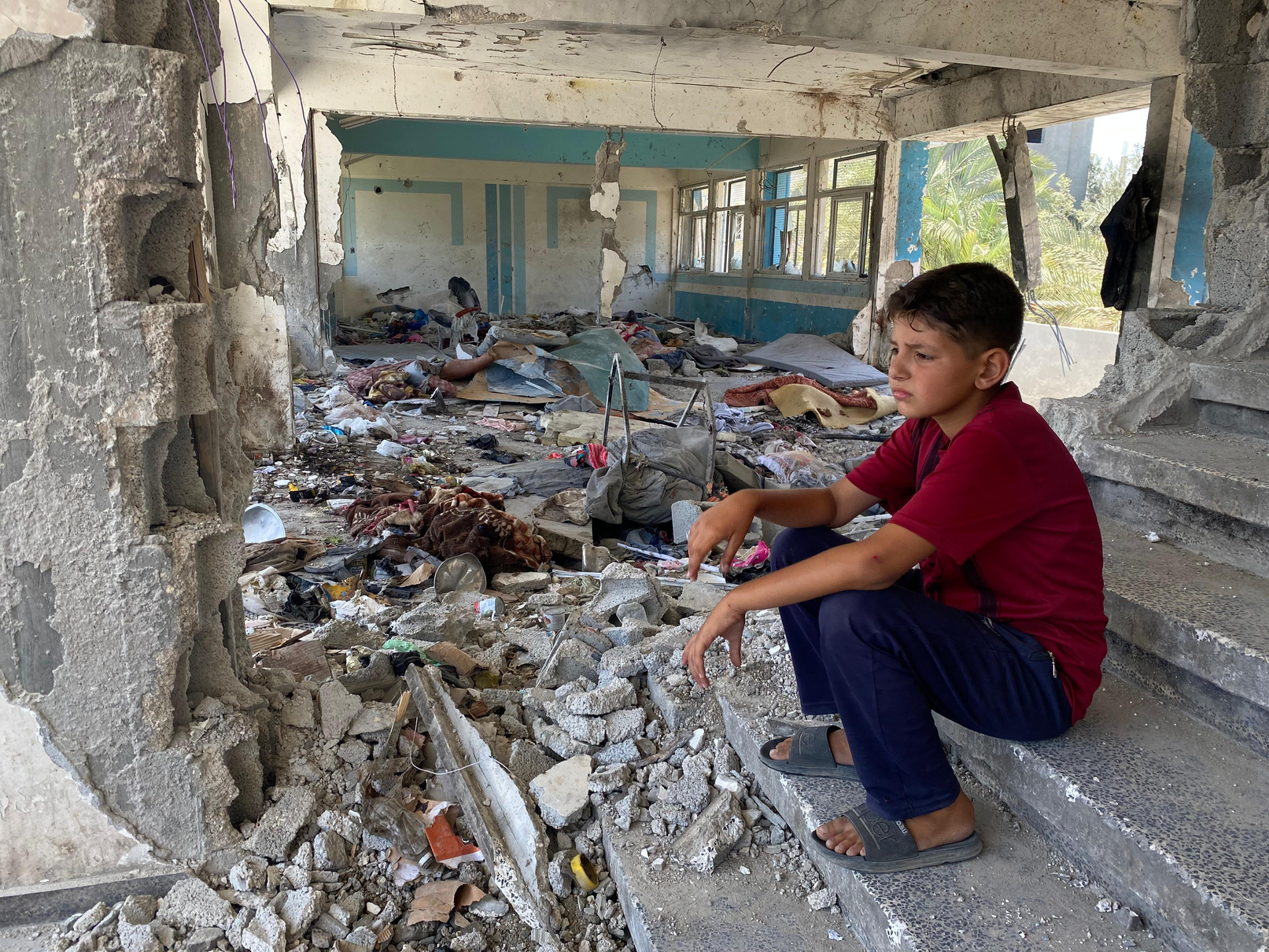 Boy sitting in the rubble of a destroyed UNRWA school in Nuseirat, Middle Areas. © 2024 UNRWA Photo